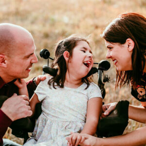 special needs child in wheelchair smiles at her parents