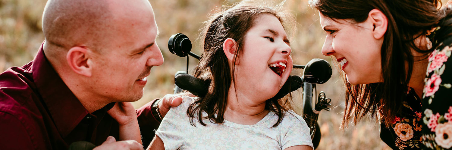close up of special needs child in wheelchair smiling at her parents