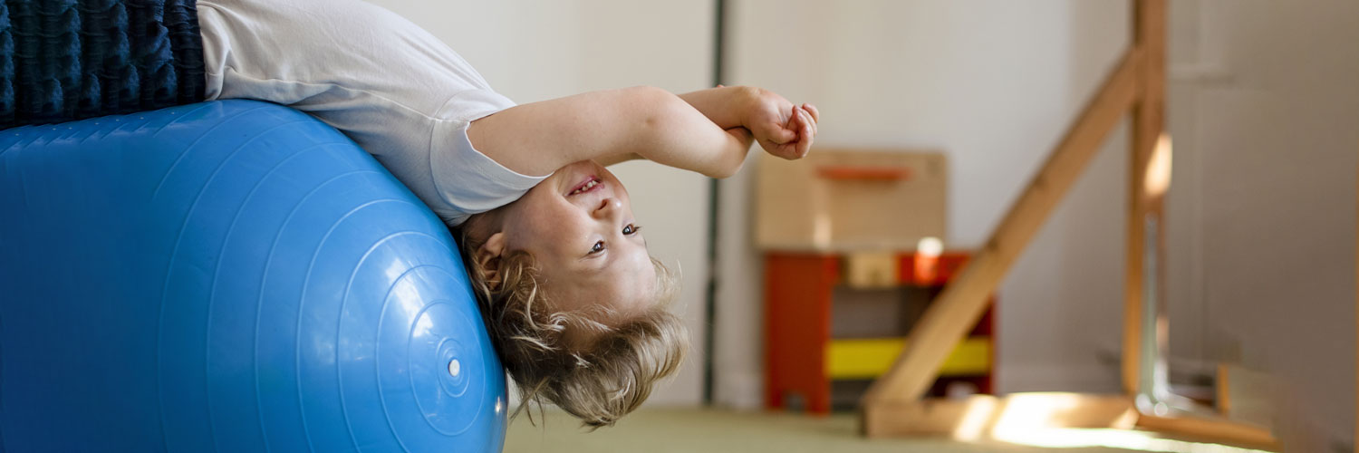 young boy leans back on a yoga ball for physical therapy All for Kids Home Health Colorado