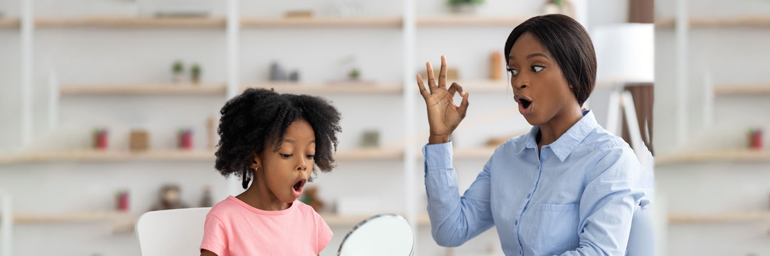 child works with speech therapist to say the letter O in a classroom setting All for Kids Home Health Colorado